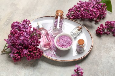 Bir şişe leylak esansı yağ, deniz tuzu ve arkaplanda çiçekler, yakın plan.