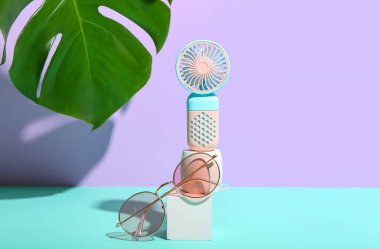 Taşınabilir elektrikli vantilatör, canavar yaprağı ve renkli gözlüklü sıva podyum.