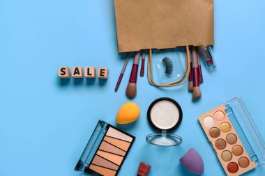 Makyaj malzemeli alışveriş çantası ve mavi arka planda metin satışı