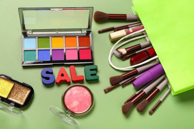 Makyaj malzemeli alışveriş çantası ve yeşil arka planda metin satışı