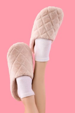 Pembe arka planda yumuşak terlikler giymiş kadın bacakları.