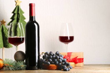 Ahşap masada Noel süslemeleri olan bir şişe ve bir kadeh şarap.
