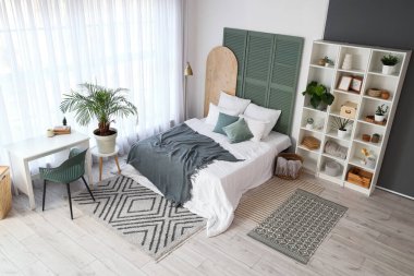 Yatak odasının içinde raf ünitesi, bitkiler ve masa var.