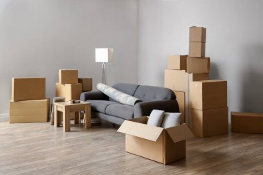 Cardboard boxes with black sofa, rolled carpet and table in living room on moving day