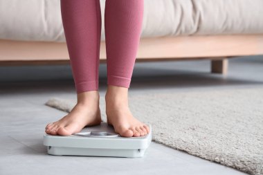 Evde terazinin üzerinde duran genç bir kadın. Kilo verme konsepti