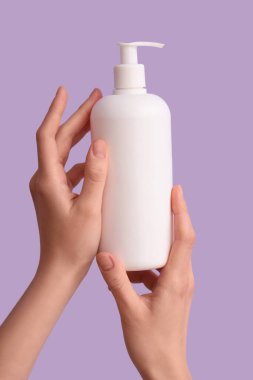 Leylak arka planında doğal krem şişesi olan kadın elleri, yakın plan.