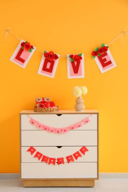 İçinde kiraz çiçekleri olan çekmeceler, hediye kutuları ve turuncu duvarın yanındaki çiçekler. Sevgililer Günü kutlaması