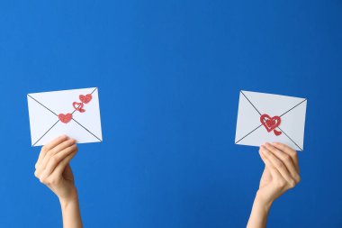 Mavi arka planda kalpleri olan kağıt zarflar tutan kadın eller. Sevgililer Günü kutlaması