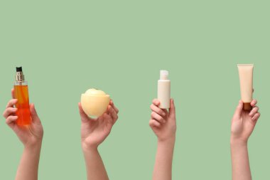 Yeşil arka planda farklı kozmetik ürünleri olan kadın elleri