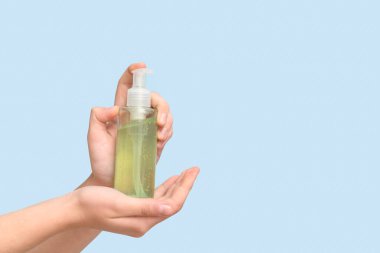 Mavi arka planda kozmetik ürünü şişesi olan kadın elleri