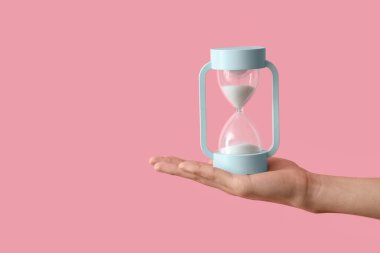 Pembe arka planda kum saati tutan kadın.