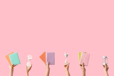 Kum saati tutan kadın eller ve pembe arka planda kitaplar.