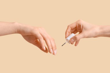 Bej arka planda tırnak eti yağı uygulayan kadın eller