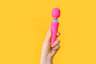 Sarı arka planda pembe vibratörlü kadın el, yakın plan.
