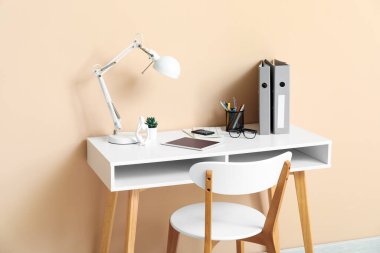 Tablet bilgisayarı, masa lambası ve bej duvarın yanında not defterleri olan rahat bir iş yeri