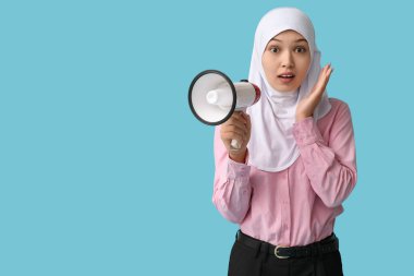 Asyalı genç Müslüman kadını mavi arka planda megafonla şoke etti. Ulusal Duyulma Günü