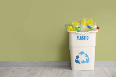 Yeşil duvarın yanında PLASTIC işareti olan tam çöp kutusu. Geri dönüşüm kavramı