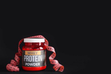 Bottle with protein powder and measuring tape on dark background
