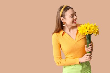 Kahverengi arka planda bir buket nergis çiçeğiyle güzel genç bir kadın.