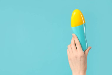 Mavi arka planda bir şişe güneş kremi ile kadın eli.