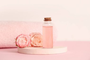 Pembe arka planda bir şişe kozmetik yağı, güller ve alçı standı