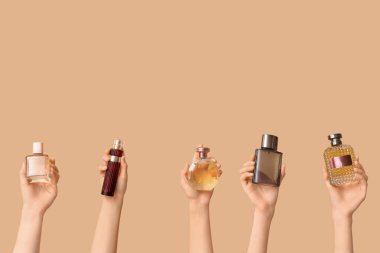 Kahverengi arka planda bir sürü parfüm şişesi olan kadın elleri.