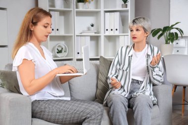 Dizüstü bilgisayarı olan kadın psikolog ve ofiste çalışan genç kız.