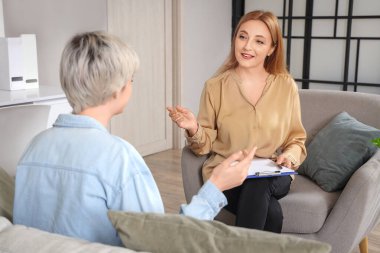 Elinde dosya olan bir kadın psikolog ofiste genç bir kızla konuşuyor.