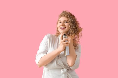 Güzel, genç, mutlu bir kadın pembe arka plana saç spreyi sıkıyor.