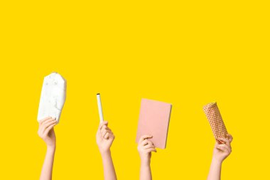 Kalem kılıflı, defterli ve sarı arka planda bir kalem hisseden kadın eller.