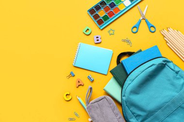 Sarı arka planda farklı kırtasiye malzemeleriyle modern okul sırt çantası.