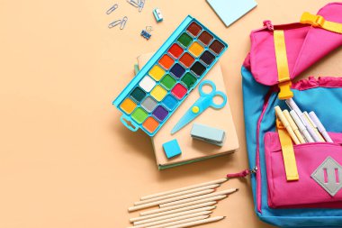 Bej arka planda farklı kırtasiye malzemesi içeren okul çantası.