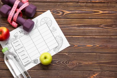 Haftalık yemek planı, bir şişe su, halterler ve tahta arka planda mezura. Diyet kavramı