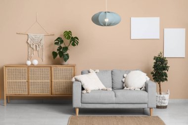 Gri kanepeli şık bir oturma odası, çekmeceler, çiçek ve asılı lamba.