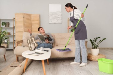 Tembel koca, karısı evde temizlik yaparken dergi okuyor.