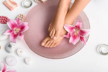 Su, orkide çiçekleri ve beyaz arka planda mumlarla spa prosedürü için kasedeki kadın bacakları.