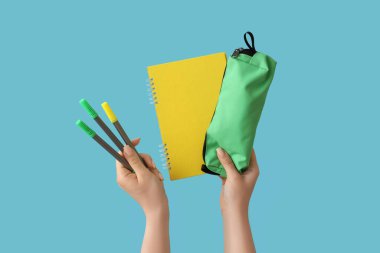 Mavi arka planda keçeli kalem, kalem kutusu ve defter olan kadın elleri