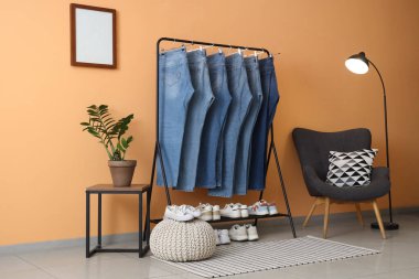 Odada bej duvarın yanında kot pantolon var.