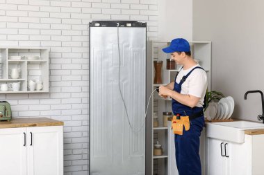 Mutfakta buzdolabını tamir eden mutlu erkek işçi.