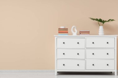 Bej duvarın yanındaki çekmecelerde yığınla kitap, canavar yaprakları ve dekor var.