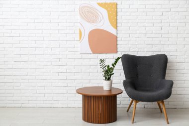 Beyaz tuğla duvara asılı resim, koltuğa ve odadaki kahve masasına.