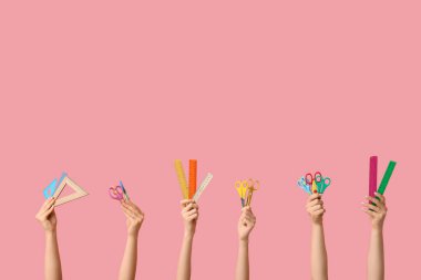 Pembe arka planda farklı okul malzemelerine sahip kadın eller.