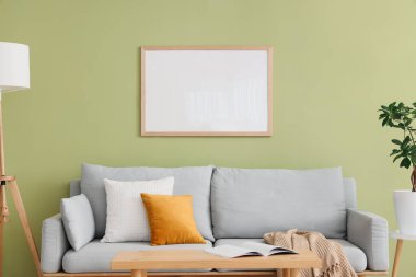 Yeşil duvarın yanındaki yastıklı şık gri kanepe.