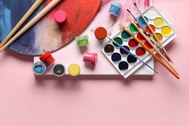 Pembe arka planda sanatçı fırçaları, boyalar, tuval ve palet