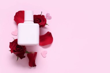 Güzel kırmızı gülleri, pembe arka planda taç yaprakları ve kalpleri olan bir şişe parfüm. Sevgililer Günü kutlaması