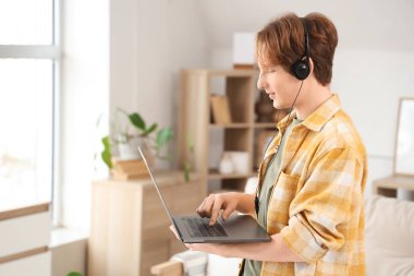 Bilgisayarı ve kulaklığı olan genç çocuk evde çalışıyor.