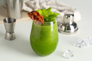 Beyaz arka planda domuz pastırması ve kereviz ile süslenmiş bir bardak Bloody Mary kokteyli.