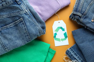 Turuncu arka planda geri dönüşüm logosu olan kıyafetler ve etiketler