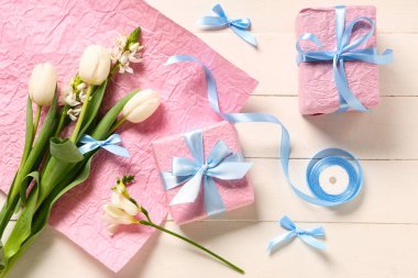 Çiçekli pembe hediye kutuları, beyaz ahşap arka planda ambalaj kağıdı ve kurdele. Uluslararası Kadınlar Günü