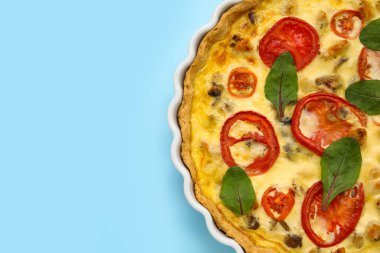 Mavi arka planda ıspanak yapraklı lezzetli domatesli tart, yakın plan.